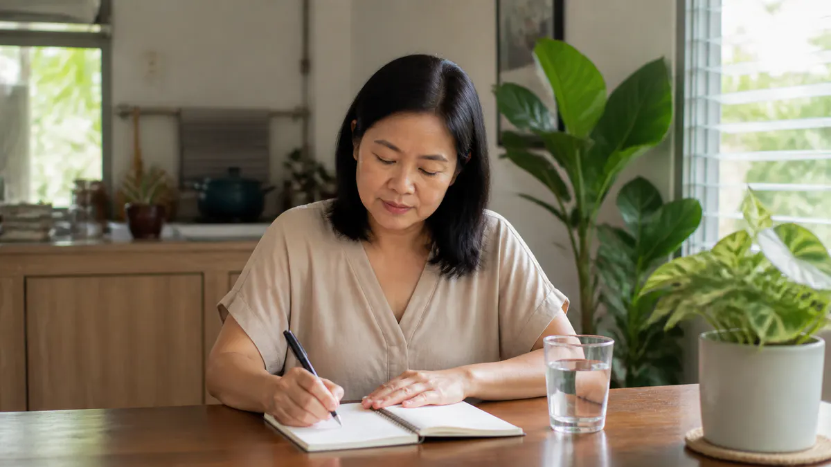 Malaysian Chinese woman recording menopause symptoms in a notebook.