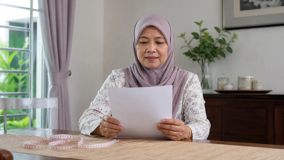Wanita Melayu menyemak senarai kesihatan dan pita pengukur.