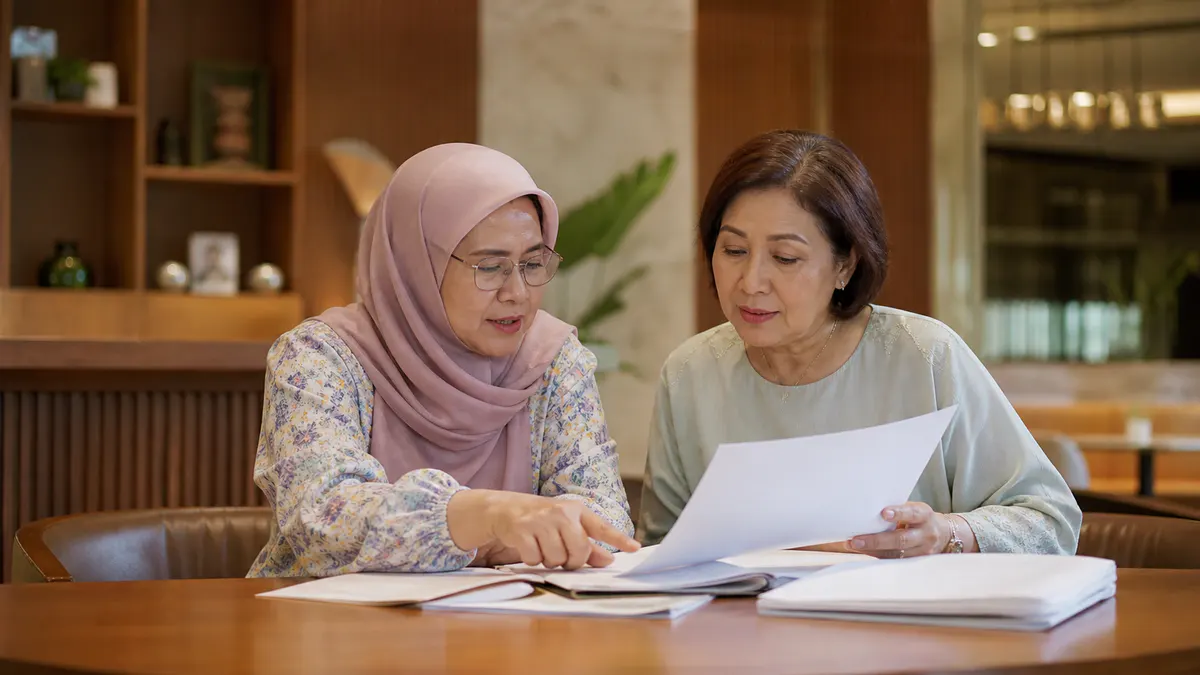 Dua wanita Melayu menyemak bahan bukti bercetak.